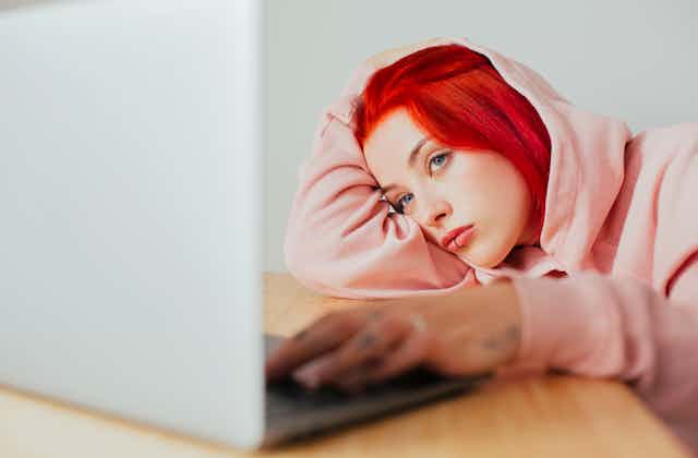 Girl with red hair and lip piercing stares at laptop