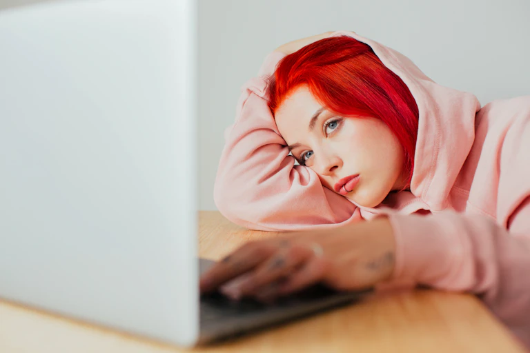 Girl with red hair and lip piercing stares at laptop
