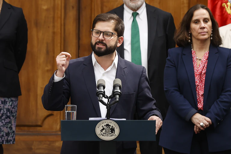 The President of Chile, Gabriel Boric gestures with his hand while making a speech at a podium flanked by ministers.
