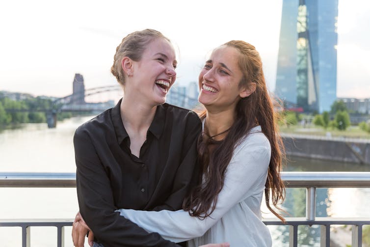 Two girls standing on the bridge laughing together.
