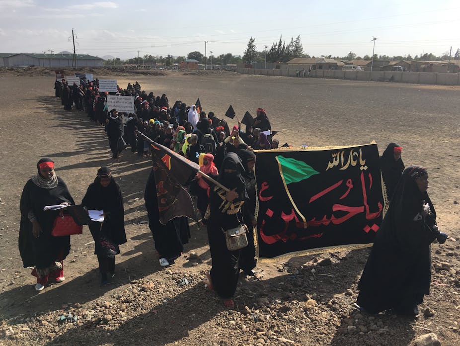 A long line of women, dressed in black, holding banners with messages in Urdu.