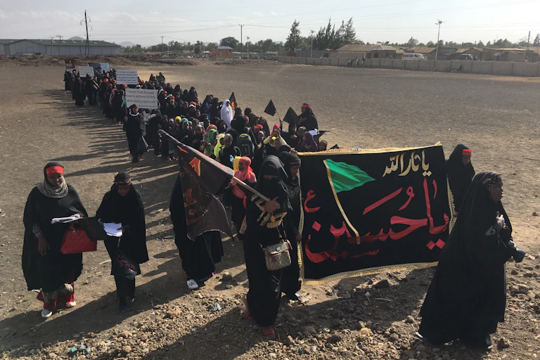 A long line of women, dressed in black, holding banners with messages in Urdu.