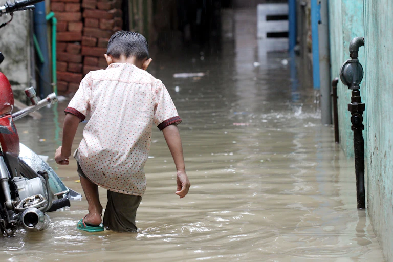 A young boy wading through knee high flood water next to a motorbike