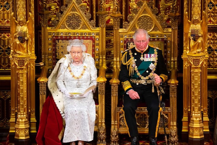 Queen Elizabeth and Prince Charles on thrones in parliament.