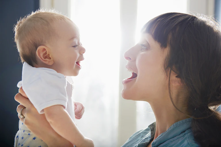 a baby and mother smiling at each other with their faces close
