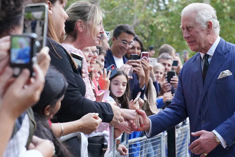 Prince Charles wearing a blue pinstripe suit shakes hands with a well-wisher.