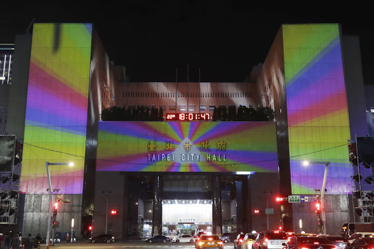 A city building illuminated with rainbow colours at night.