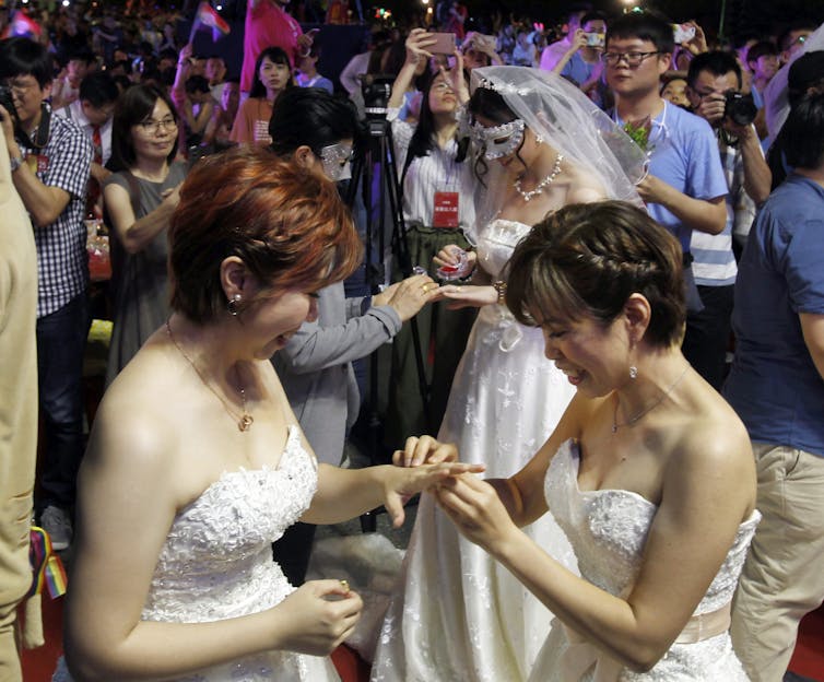 Two brides in wedding gowns exchange rings.