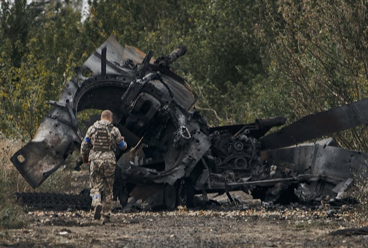 A Ukrainian soldier walking next to a burnt out Russian tank in the Kharkiv region