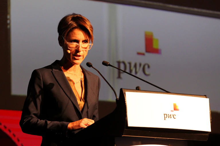 a woman stands at a podium, speaking into a microphone