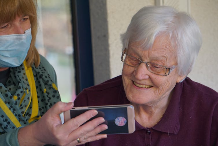 An older woman looks at a friend's phone.