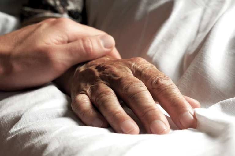 Une main jeune est posée sur une main plus âgée, reposant sur un drap blanc