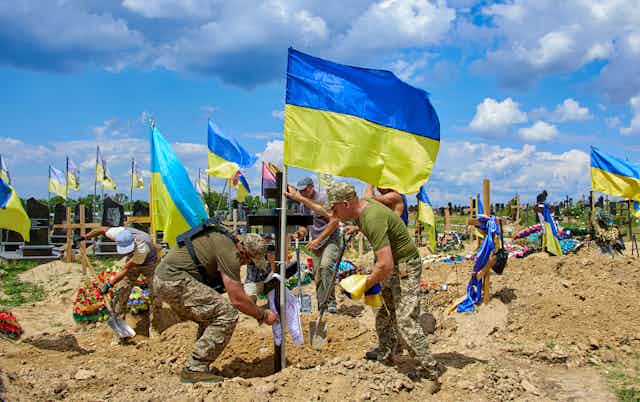 Comrades set up a national flag on the grave during a funeral in Kharkiv, June 2022.
