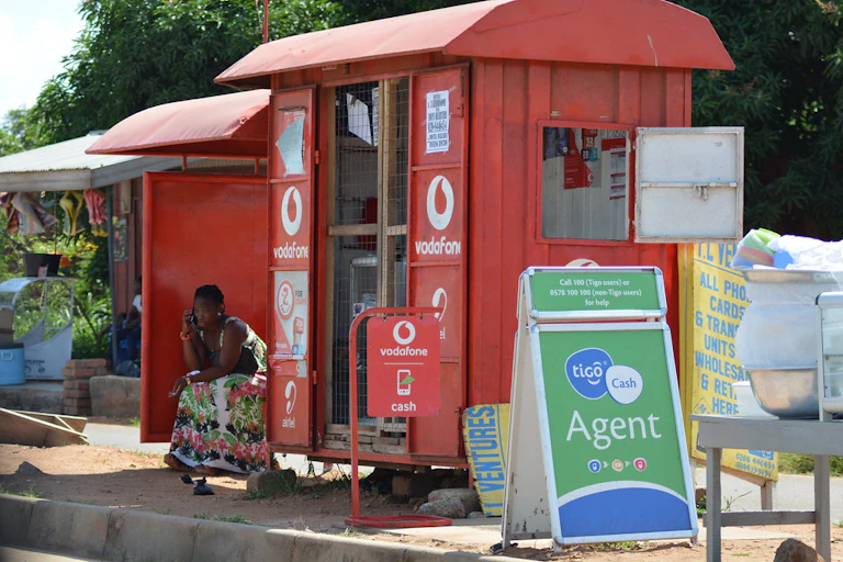 A woman sitting by a red kiosk