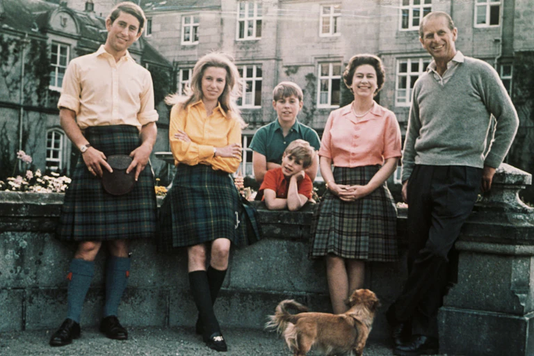 Members of the Royal family in tartan pose outdoors with a corgi.