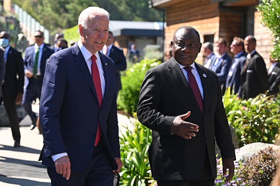 Two men wearing suits and ties chat on a stroll in a garden.