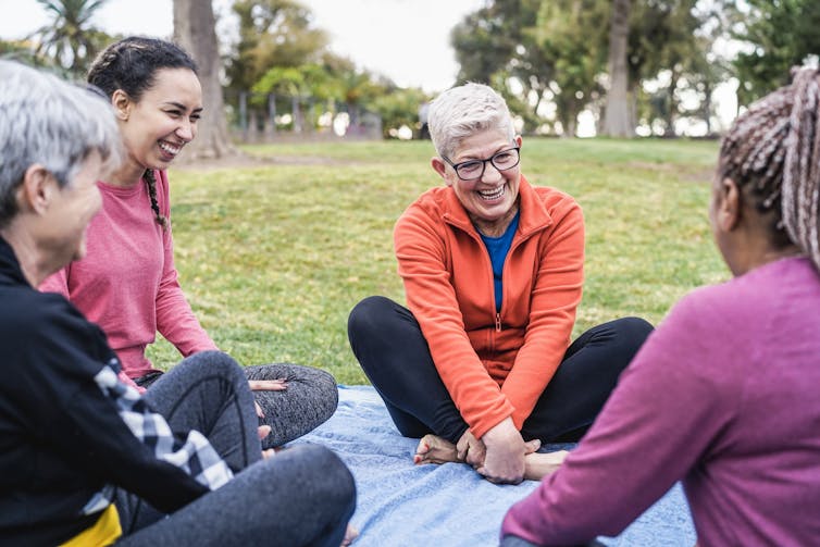 Four women of varying ages sit together on a blanket outdoors and laugh in conversation