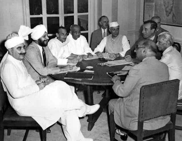 A group of men, some wearing traditional white head coverings, sit at a table