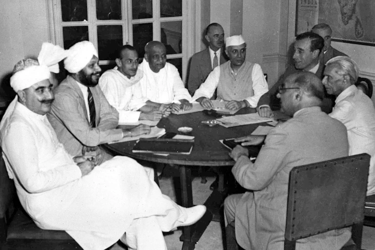 A group of men, some wearing traditional white head coverings, sit at a table