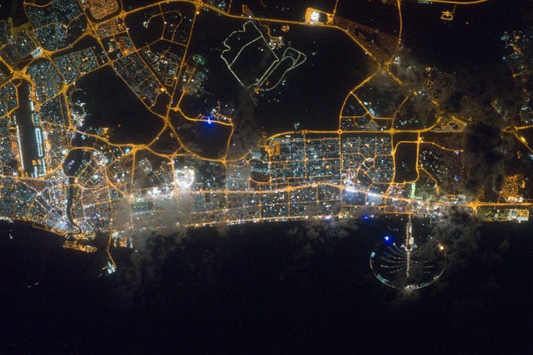 Dubai di notte, dalla ISS. Le autostrade e le strade principali sono chiaramente definite da luci giallo-arancio, mentre le aree commerciali e residenziali sono risolte in uno schema maculato di singole luci bianche, blu e giallo-arancio. NASA, CC DI