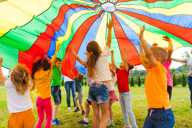 enfants jouent en dessous d'un parachute coloré