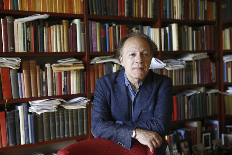 Old man in front of book-lined shelves