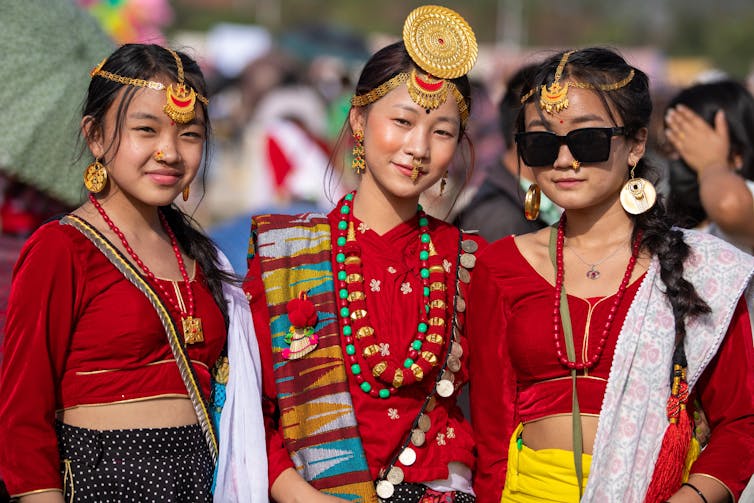 Three young women dressed in colourful Indigenous garb smile at the camera.