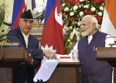 Two grey-haired men, one wearing a fez, shake hands.