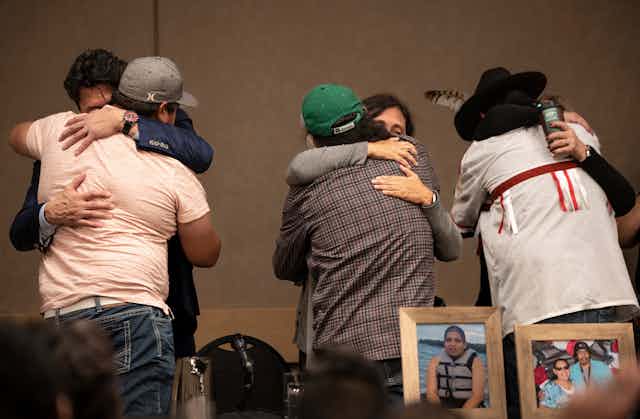 Three different pairs of people hug each other while photos of the killed victims are on a table in front of them.