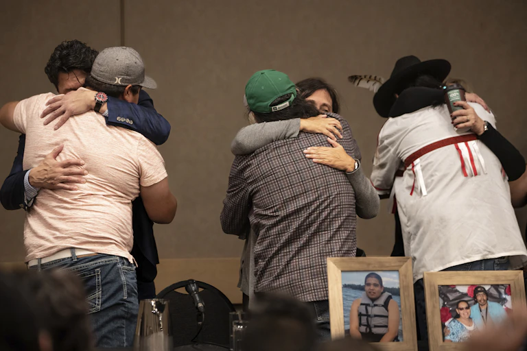 Three different pairs of people hug each other while photos of the killed victims are on a table in front of them.
