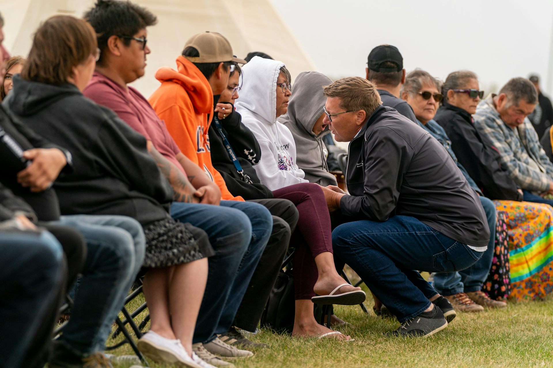 The premier squats down in front of a row of people sitting on chairs.