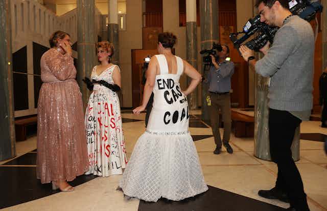 A cameraman records video of a politician wearing a gown that say "end gas and coal" across the back. 