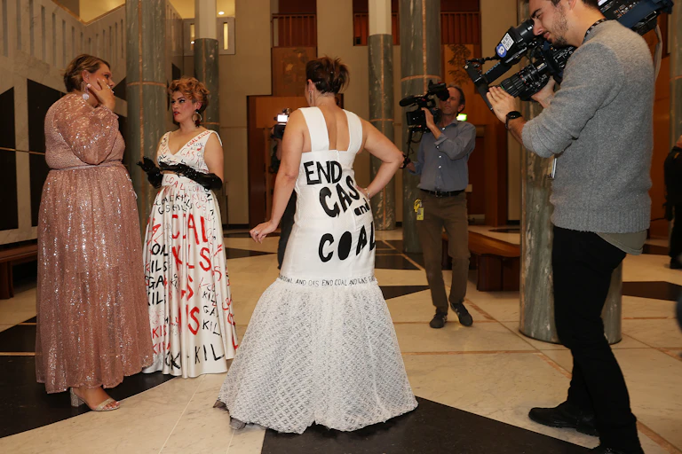 A cameraman records video of a politician wearing a gown that say "end gas and coal" across the back.