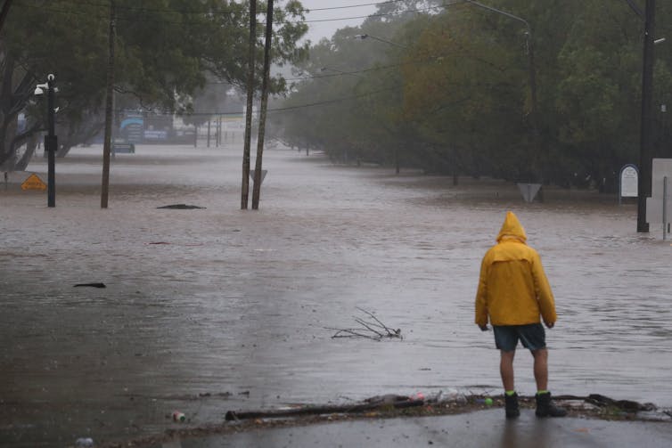 Person in yellow raincoat stands at flooded road