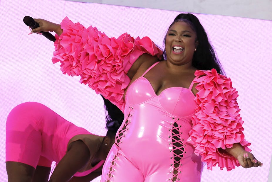 A picture of the singer, Lizzo, on stage performing. She's wearing an all-pink ensemble, and is smiling to the crowd while holding a microphone in her hand.