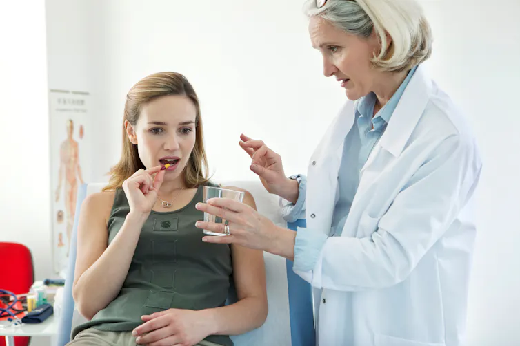 Woman in a white coat giving a patient a pill.