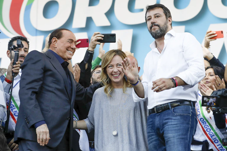 A blond woman stands between two dark-haired men at a rally.