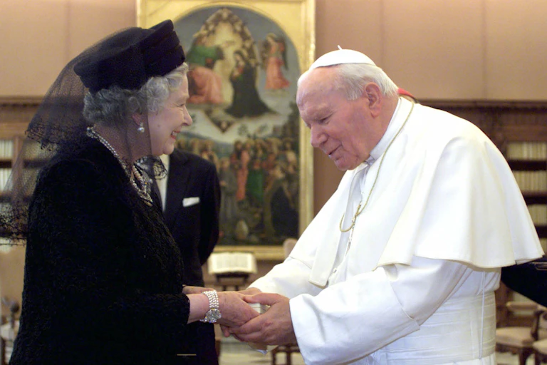 Queen Elizabeth II, dressed in black, shaking hands with Pope John Paul II in October 2000.