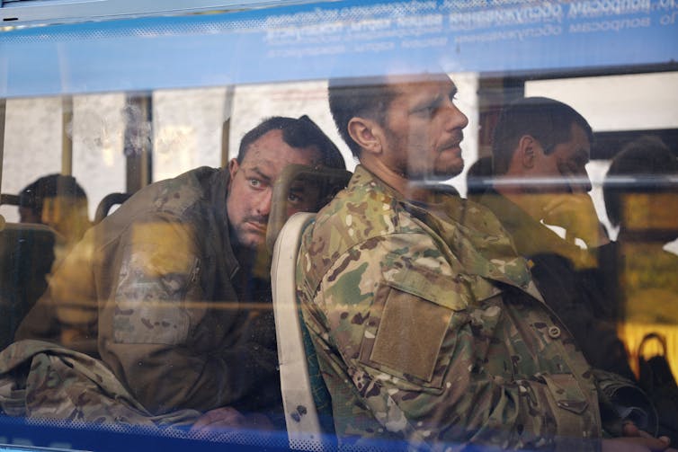 Through a window, tired men in camouflage are seen sitting.