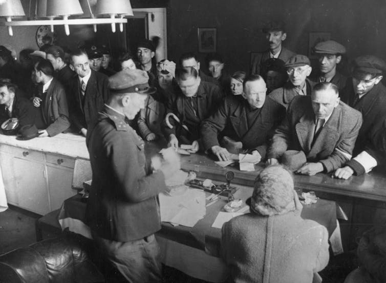 A uniformed official stands behind a desk facing a crowd of people.