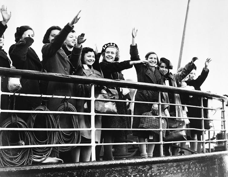 A group of young people waving while aboard a ship.