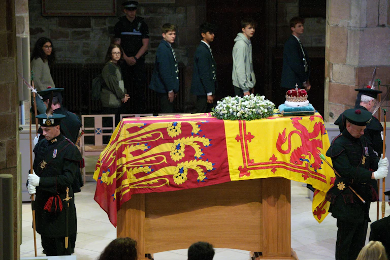 People walk past a coffin surrounded by soldiers.