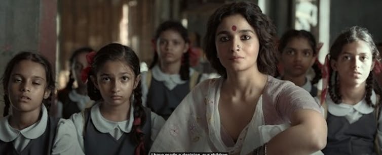 A woman is seen seated with a group of girls.