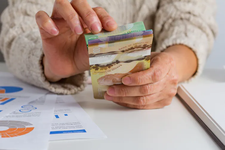 A pair of hands counting Canadian bills on a table