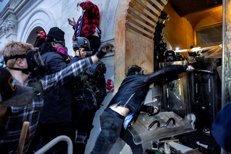 A crowd of men covered with face masks, shields and helmets clash with security forces outside the U.S. Capitol