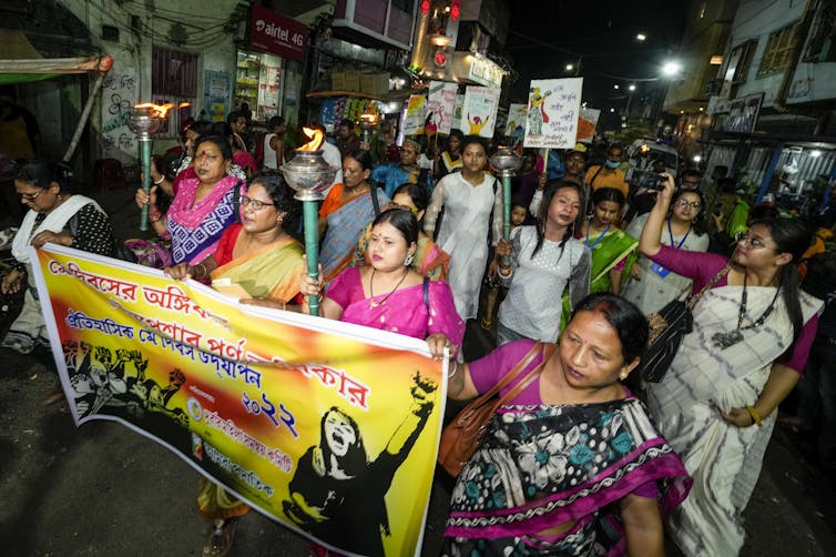 Woman march down a street holding torches, signs and banners