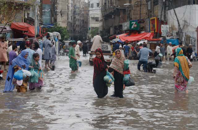 Groups of women carry plastic bags as they wade through knee-deep water in the streets of Karachi.