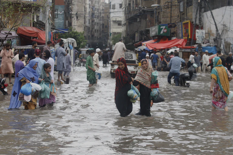 Groups of women carry plastic bags as they wade through knee-deep water in the streets of Karachi.