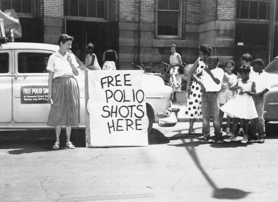An historical photo of a group of children, outside a public school, standing by a sign that says "Free Polio Shots Here."
