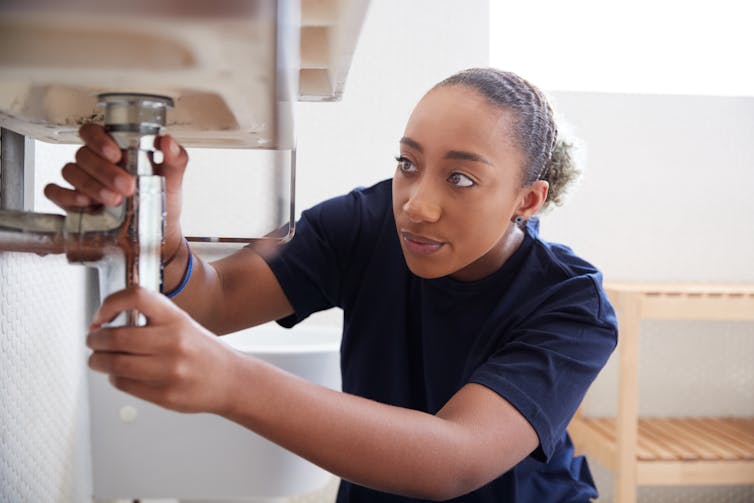 A woman fixing a sink in a bathroom.